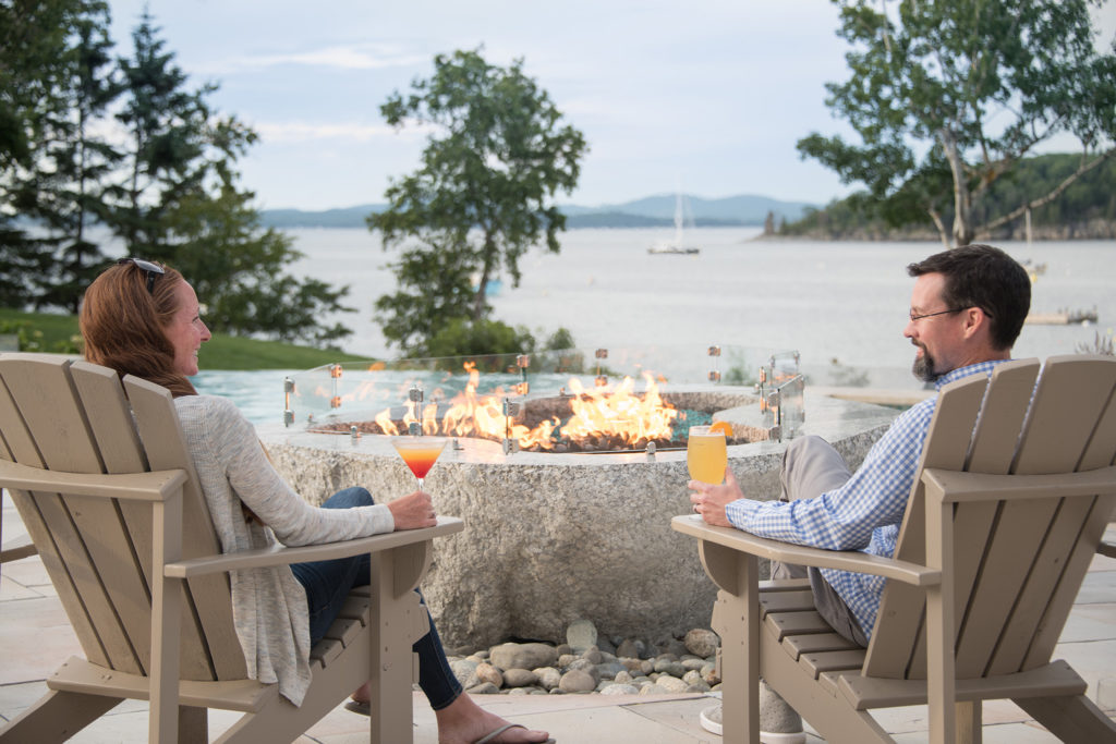Photo of a couple sitting in Adirondack chairs by the fire pit next to the pool at the Bar Harbor Inn, Bar Harbor, Maine