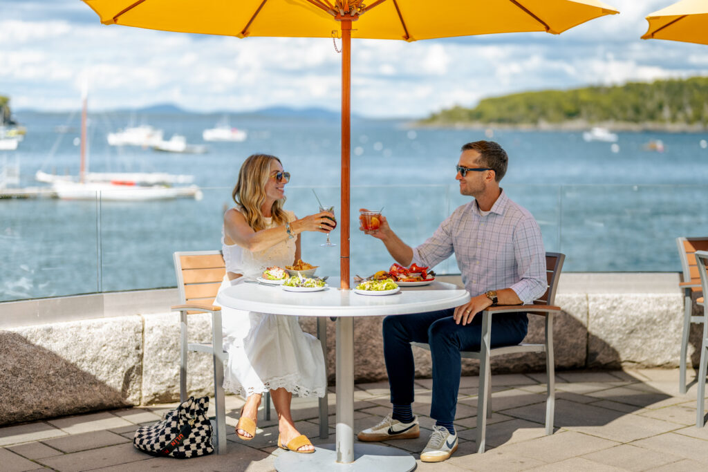 Two people dining together, toasting with the ocean in the background.